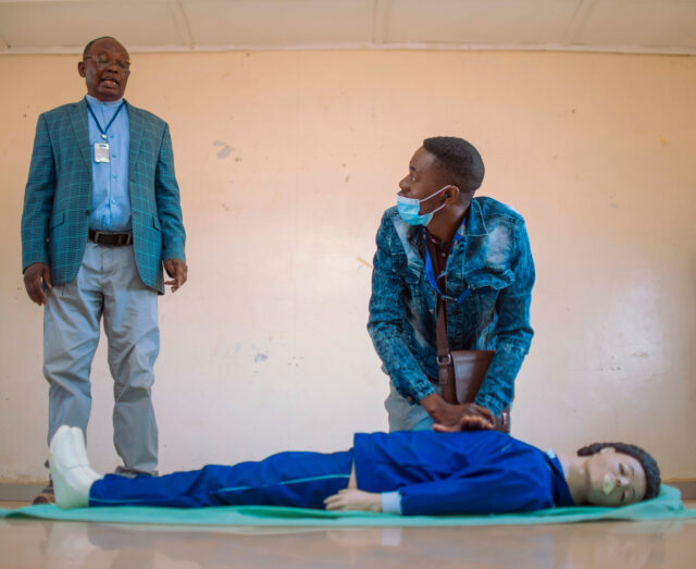 2 males standing over a manequin for first aid training
