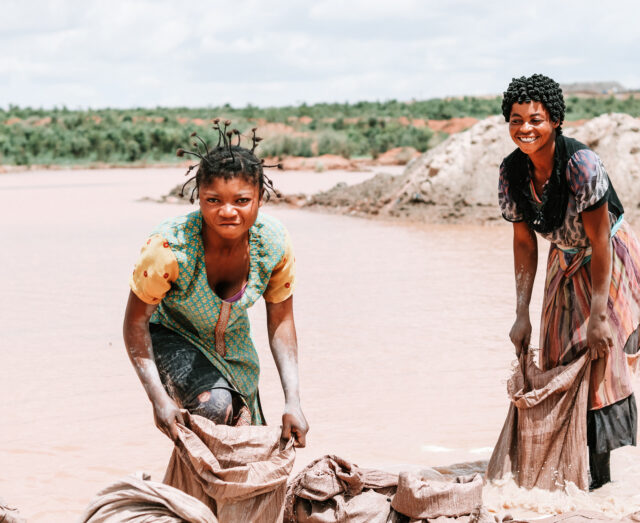 two ladies submerged barefoot in water to wash minerals before they're sold